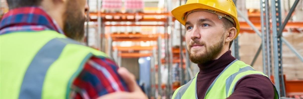 Man met helm en geel hesje legt hand op schouder mannelijke collega