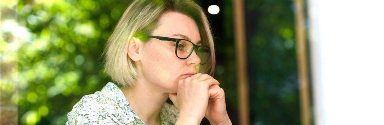 Vrouw met handen onder haar hoofd die sip voor zich uitkijkt