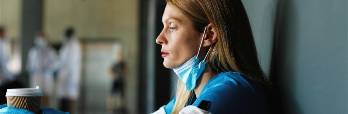 Verpleegster die op een gang zit en voor zich uit staart met koffie in haar hand